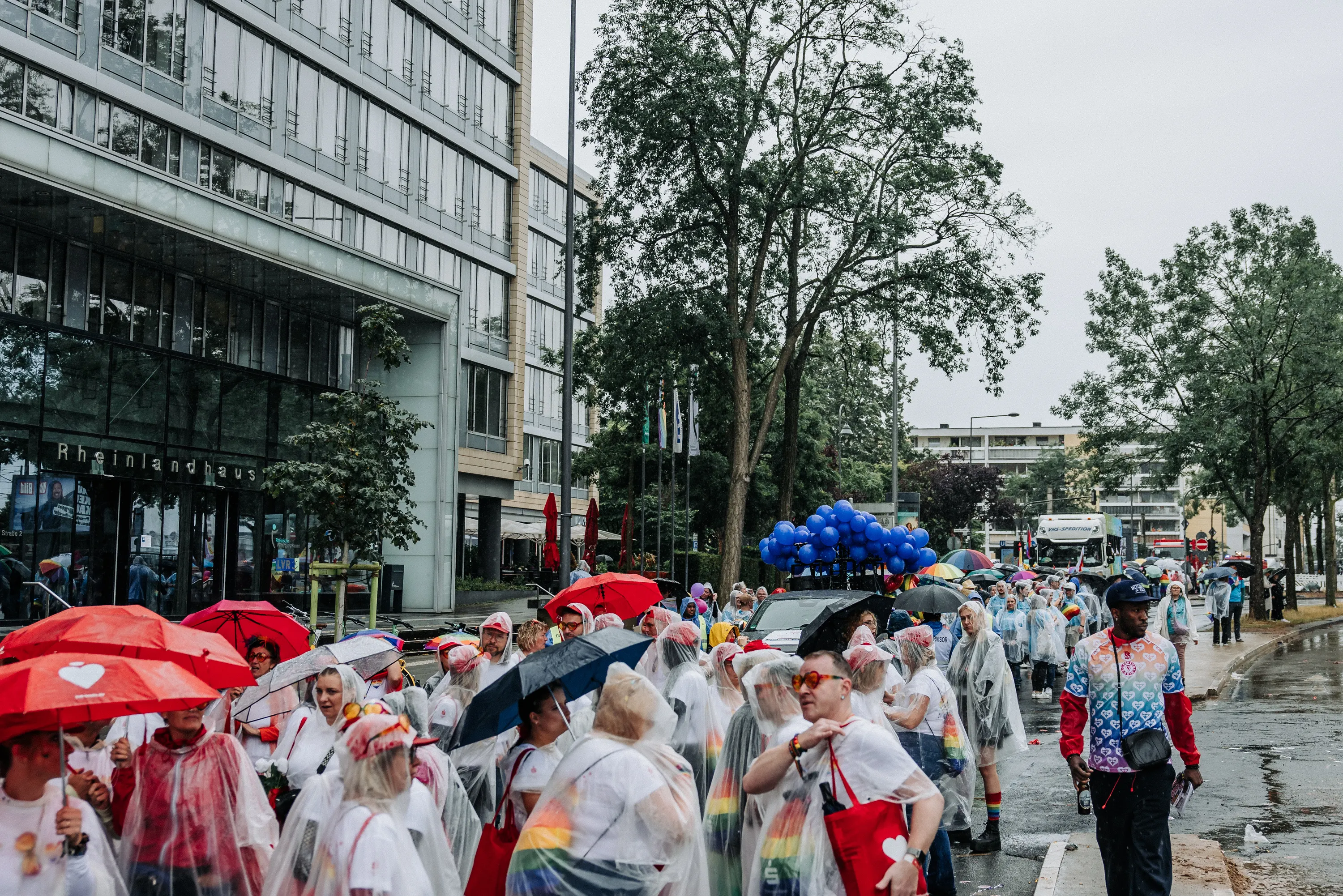 Teilnehmende der Cologne-Pride-Parade 2025 in durchsichtigen Regenponchos auf nasser Straße